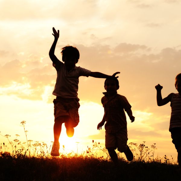 three children running and jumping and backlit by setting sun, peach and yellow colored sky