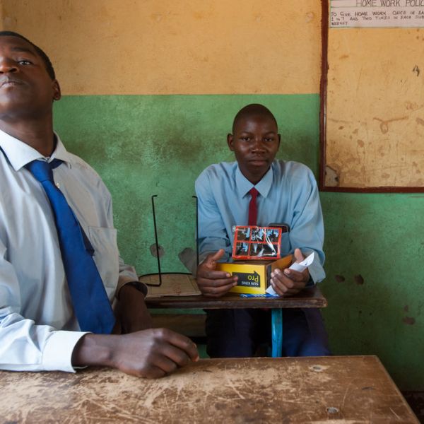 Two students in a classroom, one holds a mini solar panel while the other looks ahead