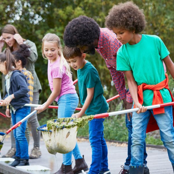 Two teachers with several students who are holding nets and peering into what is likely a body of water.