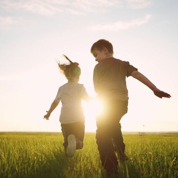 A boy and girl running on grass towards a shining sun