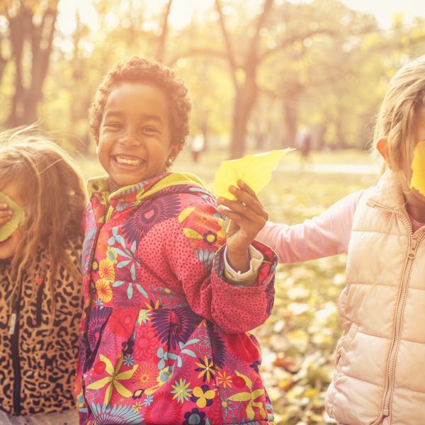 Three smiling kids in a forest filled with sunlight