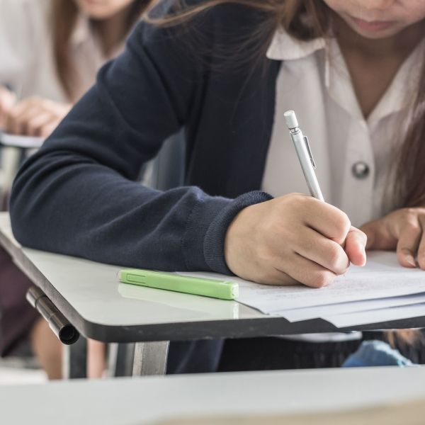 A student writes on paper at a classroom desk.