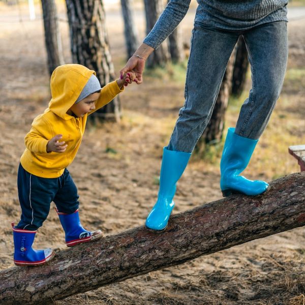 A child stands on a log while holding hands of an adult