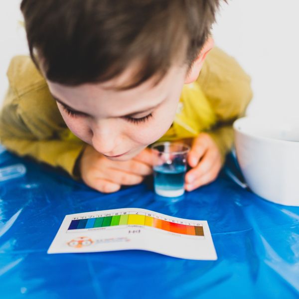 A young child hovers over a multi-colored pH result graph after completing a water pH test.