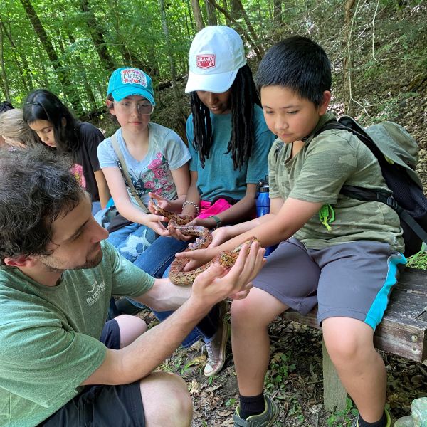 A group of young students hold a snake with guidance from an educator