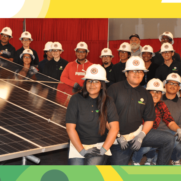 A group of people with white hard hats posing for a photo next to a large solar panel