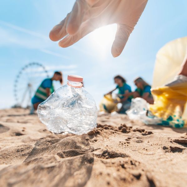 Worm's eye view of a pair of hands picking up plastic trash on beach, and in the background is a blurry group of three other volunteers and a ferris wheel