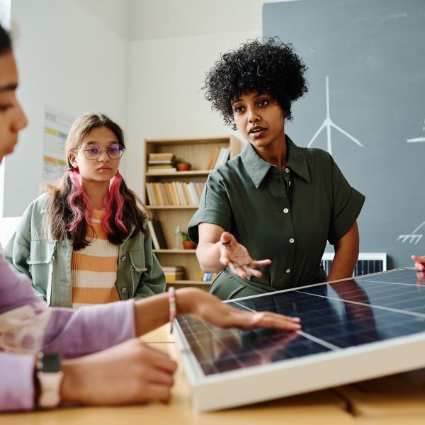 Teacher gestures at solar panels to three students