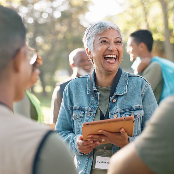 A short-haired woman with a clipboard speaks with two volunteers at a park