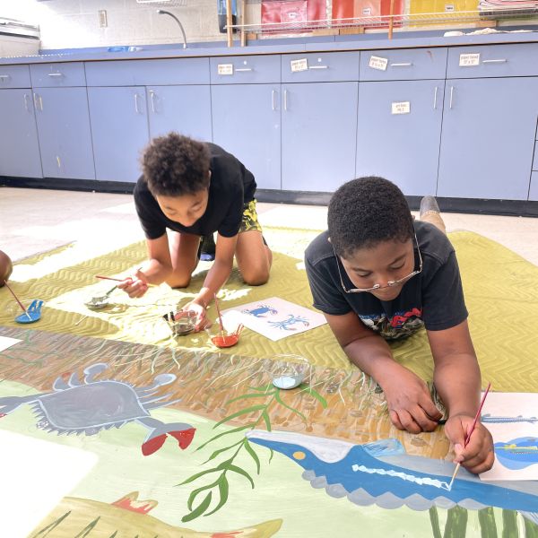 Two students paint a watershed scene in a mural