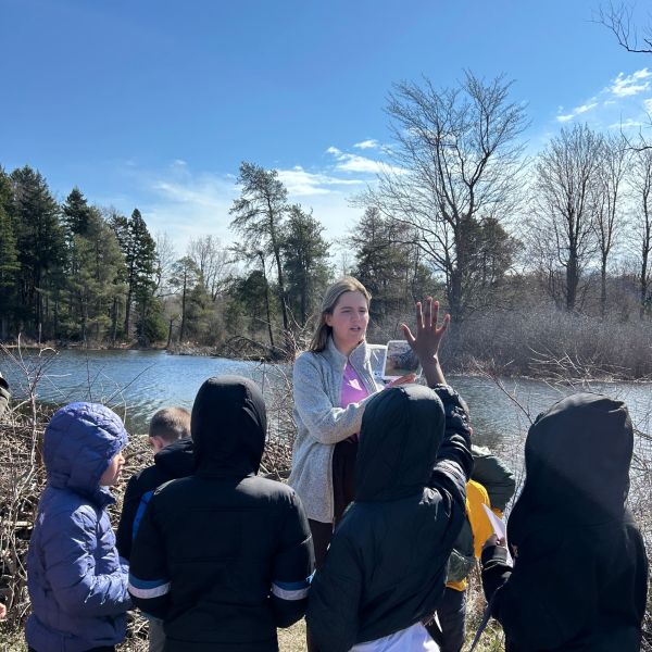Students gather around a teacher at the edge of a creek