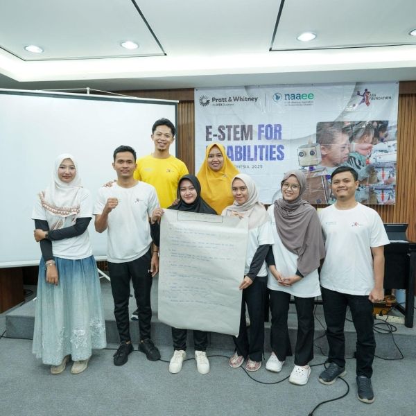 A group of people stand in front of a presentation board and banner that reads "E-STEM for Disabilities", holding up a large piece of paper 