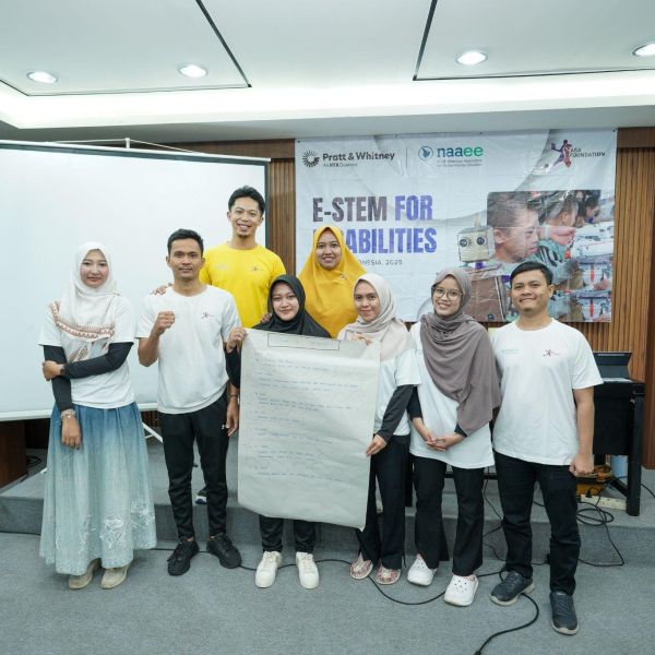 A group of people stand in front of a presentation board and banner that reads "E-STEM for Disabilities", holding up a large piece of paper 