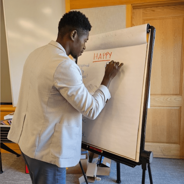 CEE-Change Fellow Jeftey writes on a large paper poster board, under the underlined word "happy."