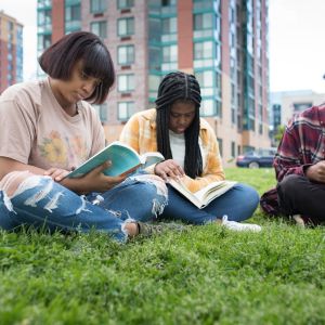 Three persons reading books while sitting on grass outside